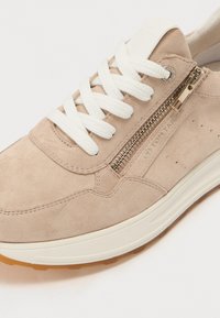 Baskets en daim beige avec lacets blancs, fermeture éclair sur le côté et semelle en caoutchouc texturé. Présente des perforations subtiles et des accents de marque sur le côté.