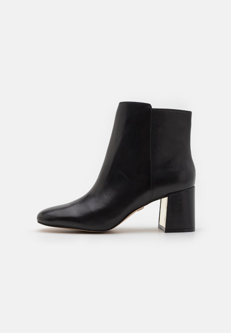 Black leather ankle boot with a pointed toe, smooth texture, and a chunky square heel featuring a metallic accent.