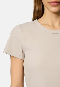 Lys beige ribbede t-shirt med korte ærmer og rund halsudskæring. Stoffet ser blødt og strækbart ud, med subtile lodrette linjer.