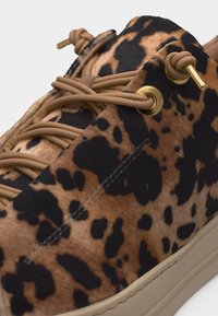 Κοντινή εικόνα καφέ και μαύρου παπουτσιού με λεοπάρ σχέδιο, με δαντέλες σε χρώμα ταμπά που περνούν από χρυσές οπές και με μπεζ λαστιχένια σόλα.