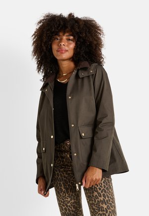 Chaqueta impermeable verde oliva con cuello de pana marrón, botones a presión y dos bolsillos frontales, combinada con pantalones de estampado de leopardo.