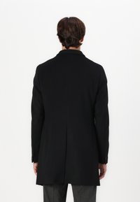 Cappotto nero con una vestibilità sartoriale, spacchetto singolo e colletto a rever. Presenta maniche lunghe e dettagli con bottoni sui polsini.
