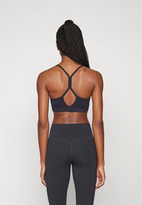 Bra desportivo preto com um design de costas cruzadas, apresentando um detalhe recortado. Combinado com leggings pretas de cintura alta, com textura suave em todo o tecido.