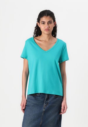 Turquoise cotton T-shirt with short sleeves and a V-neck, featuring a loose fit. Paired with a denim skirt. Smooth texture.