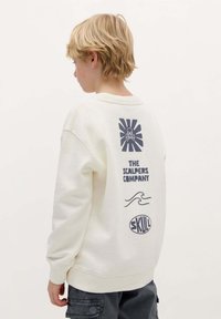 Felpa crema con vestibilità rilassata, caratterizzata da grafiche navy che includono un design a raggi di sole, testo, onde e un logo a teschio sul retro.