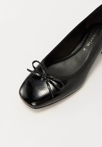 Ballerine plate en cuir verni noir avec un bout carré arrondi et un petit nœud décoratif à l'avant.