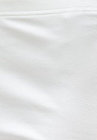 Gros plan sur un tissu blanc lisse avec des surpiqûres horizontales près du bord supérieur, montrant la texture et de légers plis.