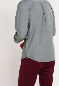 Szary longsleeve z fakturowanym wykończeniem, z centralnym plisowaniem z tyłu i zaokrąglonym dołem, w połączeniu z burgundowymi spodniami.