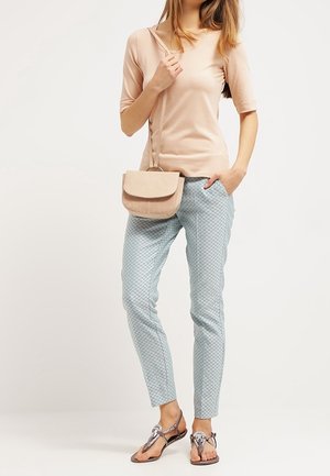 Top beige de manga corta, pantalones ajustados azul claro con estampado y sandalias metálicas. Bolso bandolera marrón con solapa curva.