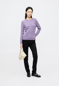 Maglione lavorato a maglia viola con motivo a treccia, pantaloni neri e mocassini neri. Porta una borsa beige. Design semplice e aderente.