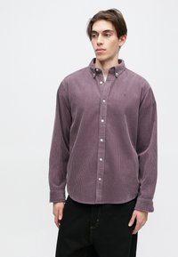 Fialová kordová košeľa s golierom na gombíky, dlhými rukávmi a bielymi gombíkovými zapínaniami. Obsahuje vertikálne jemné ryhy a zaoblený lem.