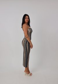 Sukienka bodycon z dzianiny, z falistym wzorem w czerni i złocie, cienkimi ramiączkami i długością do kolan. W połączeniu z białymi, wiązanymi szpilkami.