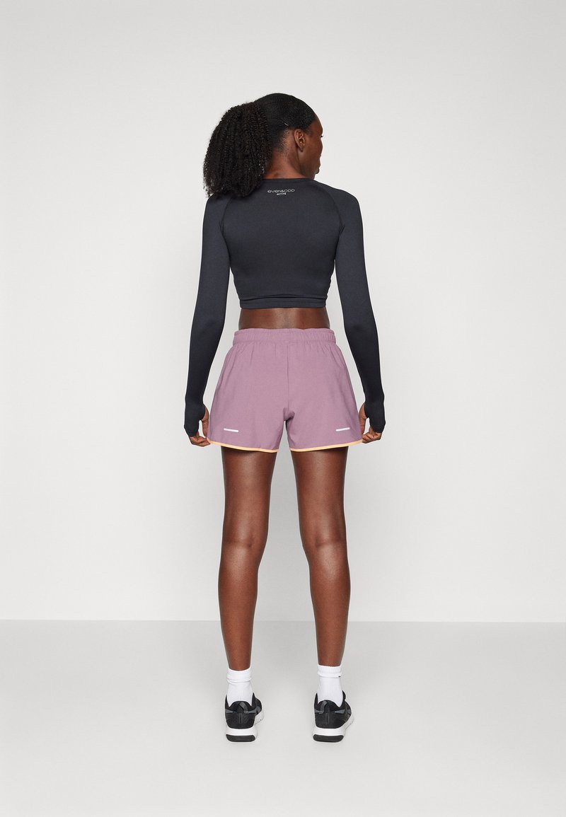 Camiseta atlética de manga larga negra y pantalones cortos lilas claros con detalles amarillos, que cuentan con una cinturilla elástica y detalles reflectantes.