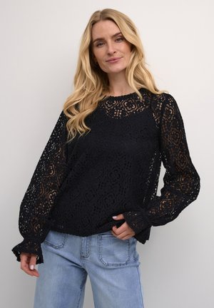 Black lace blouse with long sleeves featuring floral patterns, scalloped cuffs, and a round neckline, paired with light blue jeans.