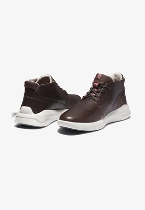 Brązowe skórzane sneakersy za kostkę z białymi podeszwami, czarnymi sznurowadłami, wyściełanym kołnierzem i perforowanymi detalami z przodu, pokazane z boku i z tyłu.