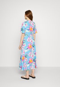 Vestido midi floral com mangas curtas, apresentando um fundo azul claro e padrões vibrantes em rosa, amarelo e verde. Inclui sandálias rasas.