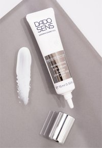 White eye cream tube with a silver accent cap. Text features “DADO SENS” and “REGENERATION.” Creamy texture shown on gray surface.