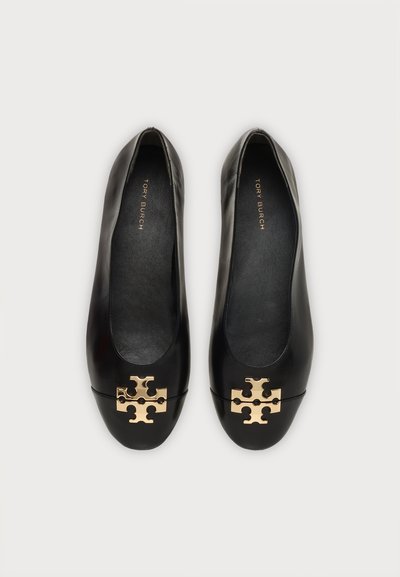 Μαύρα δερμάτινα flats Tory Burch με χρυσό λογότυπο στη μύτη, εμφανίζονται από πάνω σε ανοιχτό φόντο.