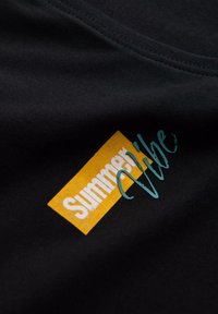 Svart tyg T-shirt med en gul rektangulär etikett med vit text "Sommar" och blå kursiv "Stämning" som överlappar. Mjuk textur.