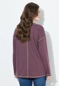Maglietta lunga viola scuro con collo rotondo, cuciture beige a contrasto e vestibilità comoda, abbinata a jeans blu.