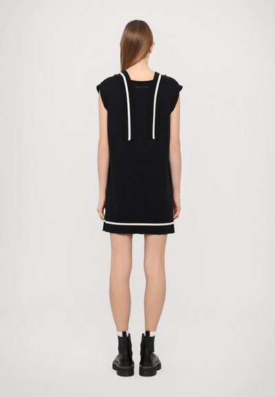 Vestido preto com mangas em forma de manga morcego, alças brancas caneladas e riscas horizontais contrastantes na barra. Combinado com botins pretos.