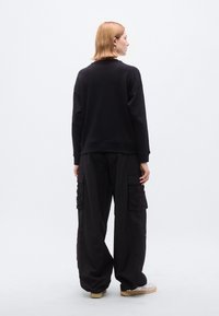 Μαύρο φαρδύ φούτερ με στρογγυλή λαιμόκοψη, συνδυασμένο με άνετο μαύρο παντελόνι cargo με πολλές τσέπες και χαλαρή εφαρμογή.