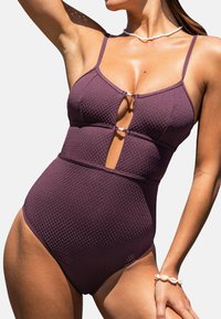 Maillot de bain une pièce bordeaux avec un motif texturé, des bretelles réglables et un détail découpé au niveau du buste. Il présente un design à rayures.