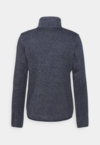 Tummansininen, pitkähihaisuus takki, jossa on korkea kaulus. Teksturoitu kangas sisältää hienovaraisen kuvion, ja siinä on ommeltuja saumoja sekä suora helma.