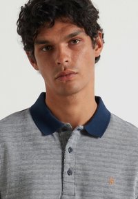 Polo a maniche corte di colore azzurro con un motivo a righe. Presenta un colletto blu navy e una chiusura con tre bottoni. Piccolo logo sul petto.