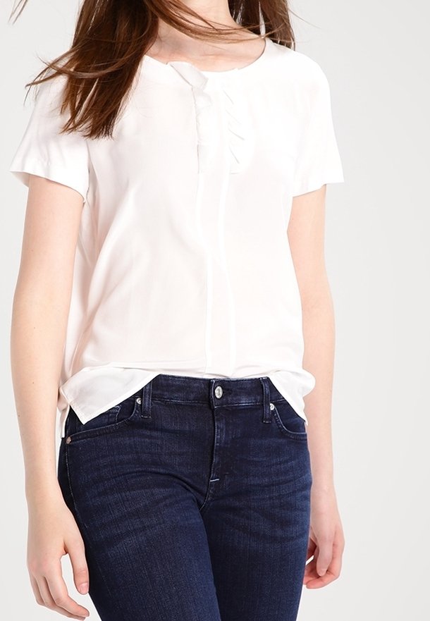 Blusa bianca a maniche corte con scollatura tonda e dettagli di pieghe verticali, abbinata a jeans in denim blu scuro. Tessuto liscio e leggero.