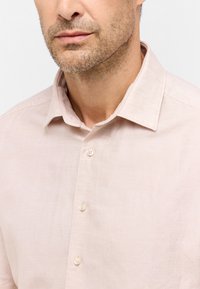 Lichtroze linnen shirt met een button-down kraag, voorzien van een subtiele textuur en duidelijke plastic knopen langs de knoopsluiting.