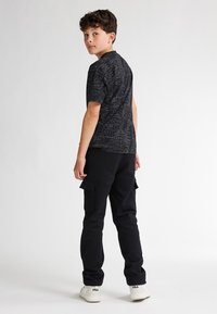 Zwarte t-shirt met een gestructureerde grafische print, gecombineerd met zwarte cargobroek met zakken. Witte sneakers maken de outfit compleet.