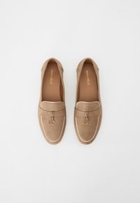 Beige loafers made of soft suede with a stitched accent, decorative charm, and a smooth sole. Flat design for easy wear.