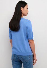 Blauwe korte mouw trui met een ronde hals, zachte textuur en geribbelde rand, gecombineerd met nauwsluitende spijkerbroek in medium-was.