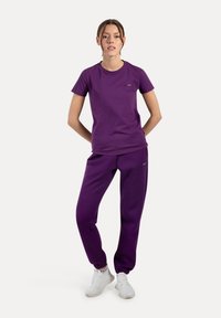Camiseta de algodón morada y pantalones a juego, diseño ajustado con mangas cortas, cintura elástica y tobillos ajustados. Se aprecia un detalle de marca sencillo.