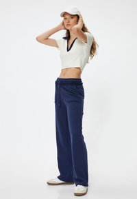 Marineblauwe sweatpants met een tailleband met trekkoord, gecombineerd met een witte geribbelde crop top met een marineblauwe kraag, en witte schoenen.