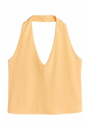 Žena v slamennom klobúku, s žltým tielkom bez rukávov, zelených pruhovaných nohaviciach a sandáloch kráča po zakrivenej pobrežnej ceste s oceánom a loďou v pozadí.