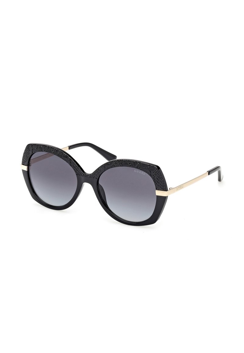 Gafas de sol negras con montura oversized, lentes oscuros en degradé, detalles texturizados en negro en la parte superior y acentos dorados en los laterales.