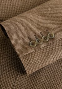 Manche de blazer pied-de-poule marron avec quatre boutons bruns translucides cousus en ligne près du poignet.