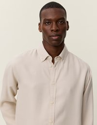 Μέ beige πουκάμισο με κουμπιά, δομημένο γιακά και μακριά μανίκια. Κατασκευασμένο από απαλό ύφασμα, με διακριτή υφή και κανονικό κουμπί.