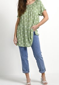 Zielona kwiatowa tunika o luźnym kroju, z krótkimi rękawami i marszczonym dekoltem. Do tego jasne, podwinięte jeansy i białe sandały.