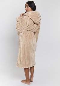 Accappatoio beige in morbida peluche con cappuccio, texture a coste e cintura legata in vita, finitura morbida e design al ginocchio.