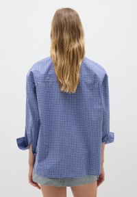 Camicia a quadri blu e bianca con maniche tre quarti, tessuto morbido, vestibilità rilassata e maniche arrotolate, vista da dietro.