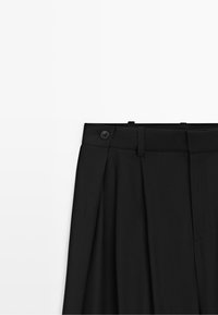 Zwarte geplooide rok met hoge taille, riemlussen en een knoopsluiting in de tailleband, weergegeven tegen een witte achtergrond.