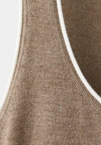Gros plan d'un tissu tricoté marron avec une bordure blanche sur le bord, montrant la texture détaillée et le motif des points.