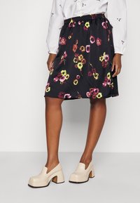 Jupe florale noire ornée de fleurs multicolores vives, avec une taille élastique et une coupe au genou, assortie à des chaussures à talons carrés crème.