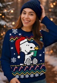 Navy blue Christmas sweater featuring Snoopy in a Santa hat holding a green gift, with white snowflakes and a zigzag candy cane pattern.