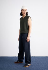 Green ribbed sleeveless knit top paired with navy sweatpants and black sneakers. Noticeable white stripes on the shoes and a white beanie.