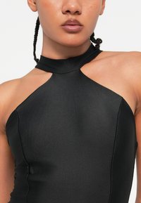 Juoda halter tipo suknelė su prigludusia liemene, kuri turi išpjovimus pečių srityje. Lygus tekstūras ir elegantiškas dizainas.