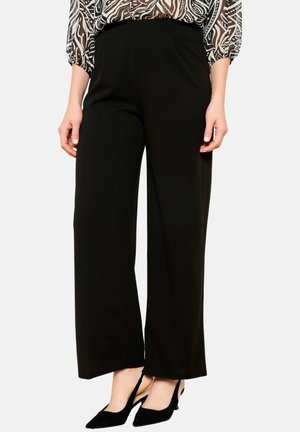 Pantalons larges noirs avec une texture lisse et douce. Dotés d'une taille haute et associés à des chaussures noires à bouts pointus. Design simple et élégant.
